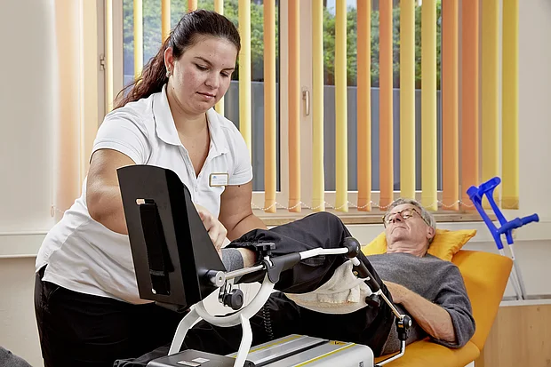 Therapeutin behandelt einen Patienten auf der Therapieliege mit einer Bewegungsschiene