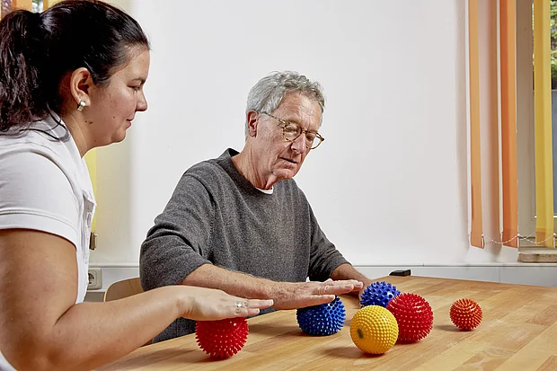 Therapeutin übt mit einem älteren Patienten die Handmotorik mit bunten Igelbällen